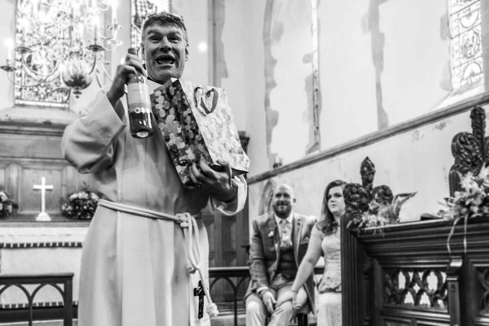 Priest with a bottle of wine during wedding celebration by piccolinoweddings