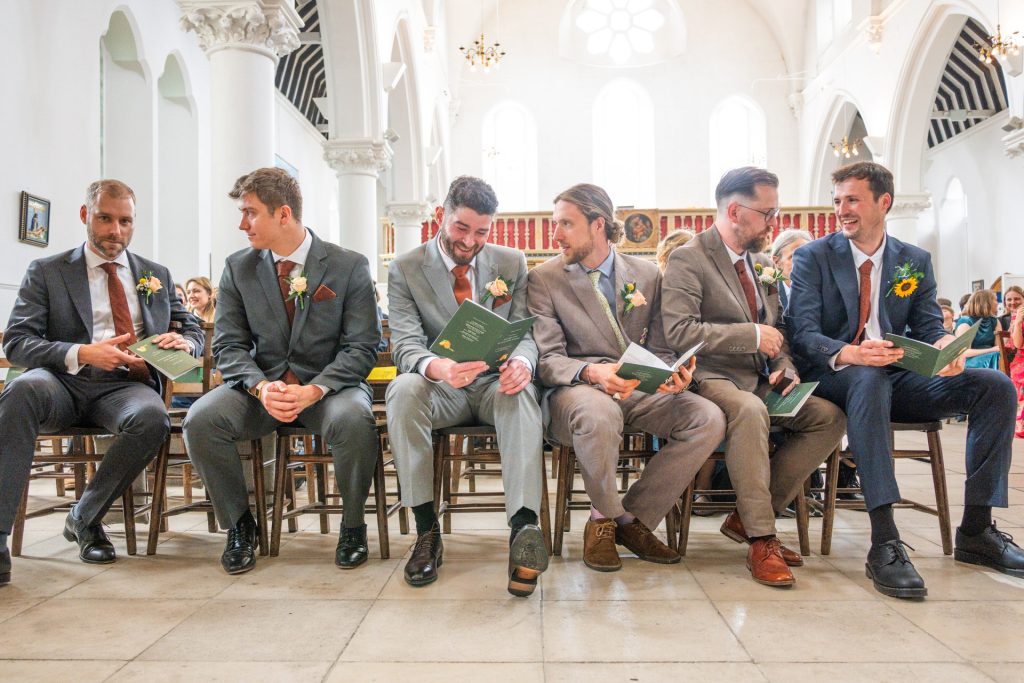 Groomsmen in mismatched suits sitting together and laughing before the ceremony at St John's Church, Dulwich
