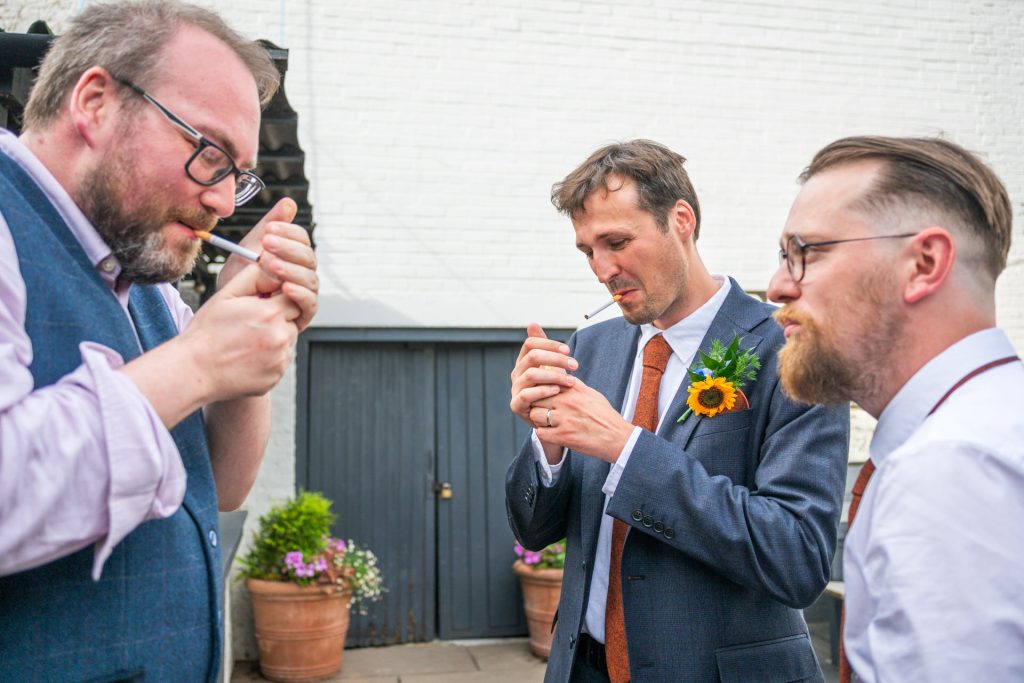 Groomsmen sharing a quiet moment outside The Lordship Pub, Dulwich, one wearing a sunflower buttonhole