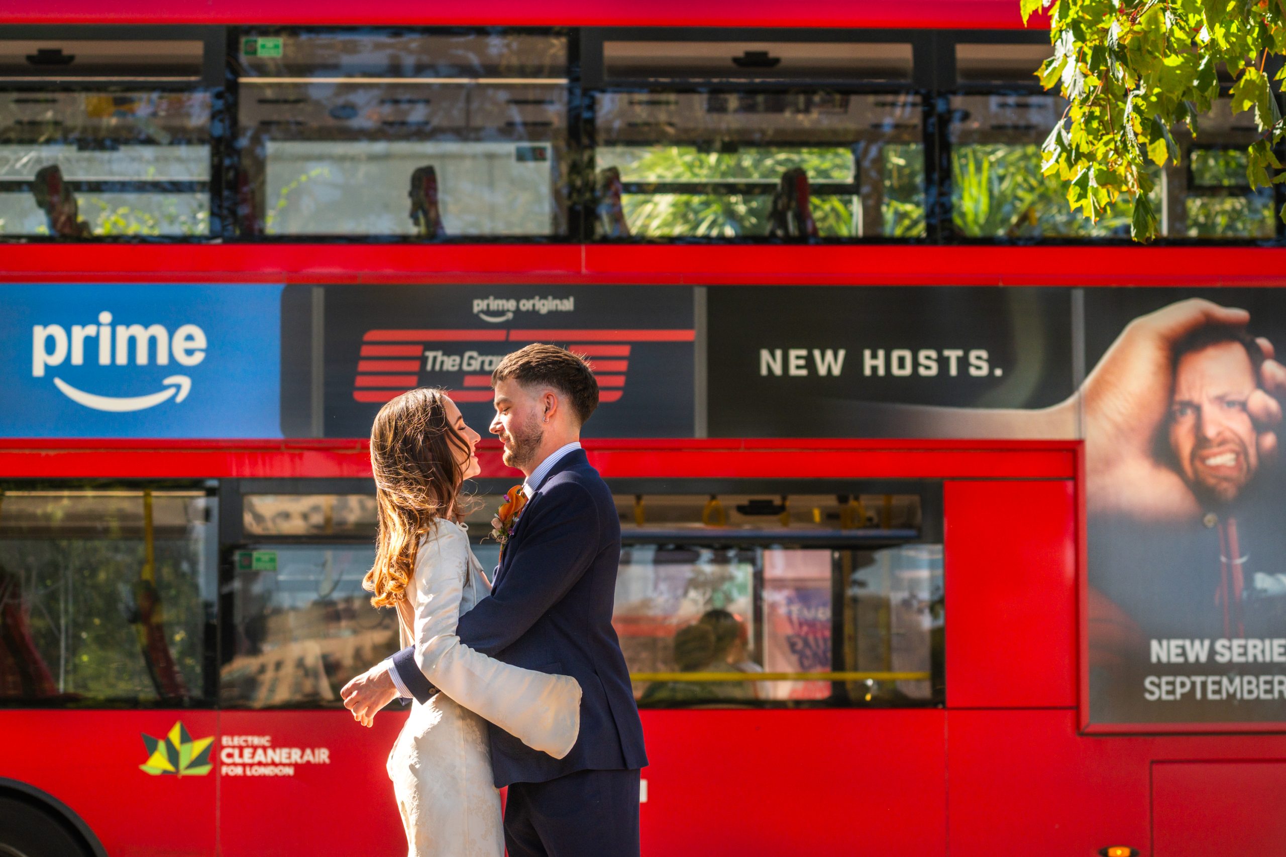 Bride and groom embracing in front of a red London double-decker bus on a sunny day, London Wedding photographer, documentary wedding photography