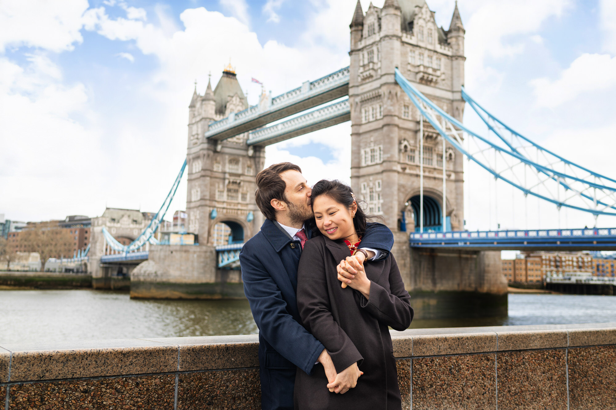 Couple embracing in front of Tower Bridge with the man kissing his partner’s head, London Wedding photographer, documentary wedding photography